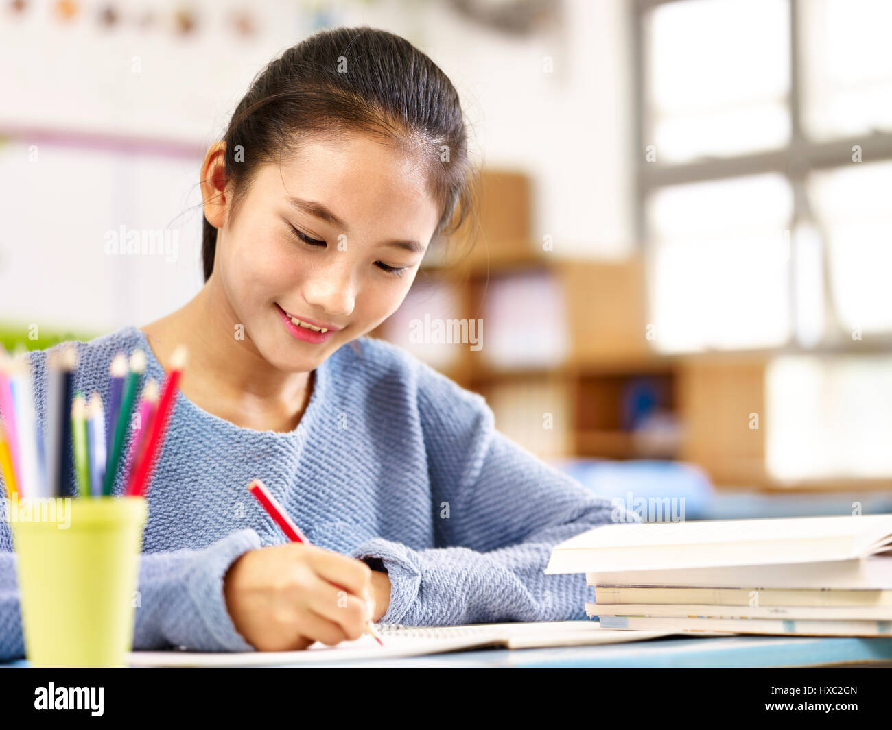 11 Jahre alte asiatische Schulmädchen Hausaufgaben, glücklich und lächelnd. Stockfoto