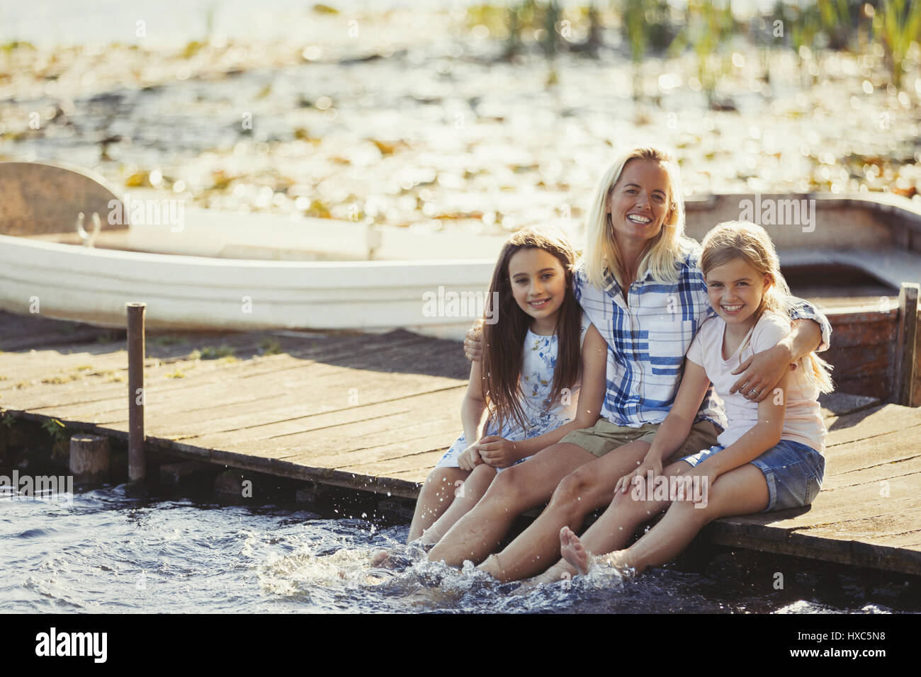 Porträt glückliche Mutter und Töchter auf Dock, die Füße im See plantschen Stockfoto