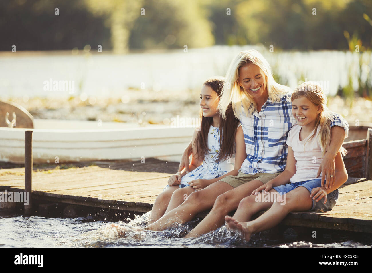 Lächelnd, liebevolle Mutter und Töchter auf Dock, die Füße im See plantschen Stockfoto