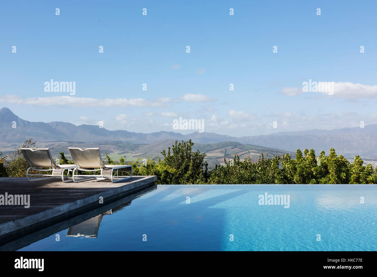 Luxus Infinity Pool und Liegestühlen mit Blick auf die Berge unter sonnig, blauer Himmel Stockfoto