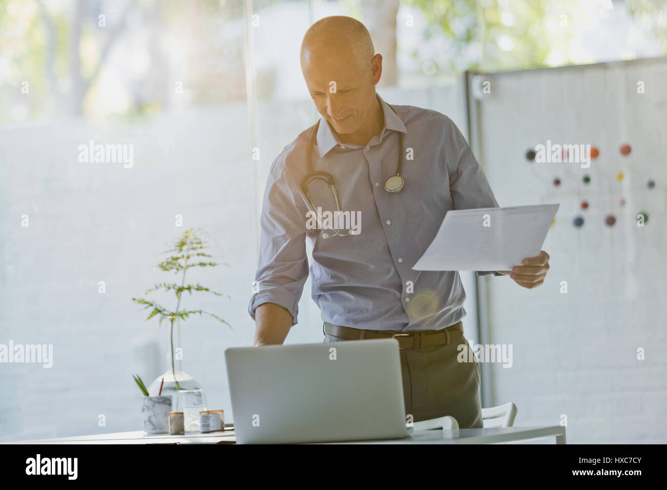 Männlichen Arzt mit Papierkram stehen am Laptop in Arztpraxis Stockfoto