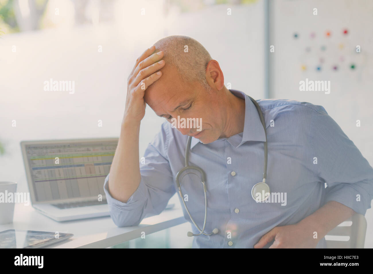 Müde, gestresst männlichen Arzt mit Kopf in Händen in Arztpraxis Stockfoto