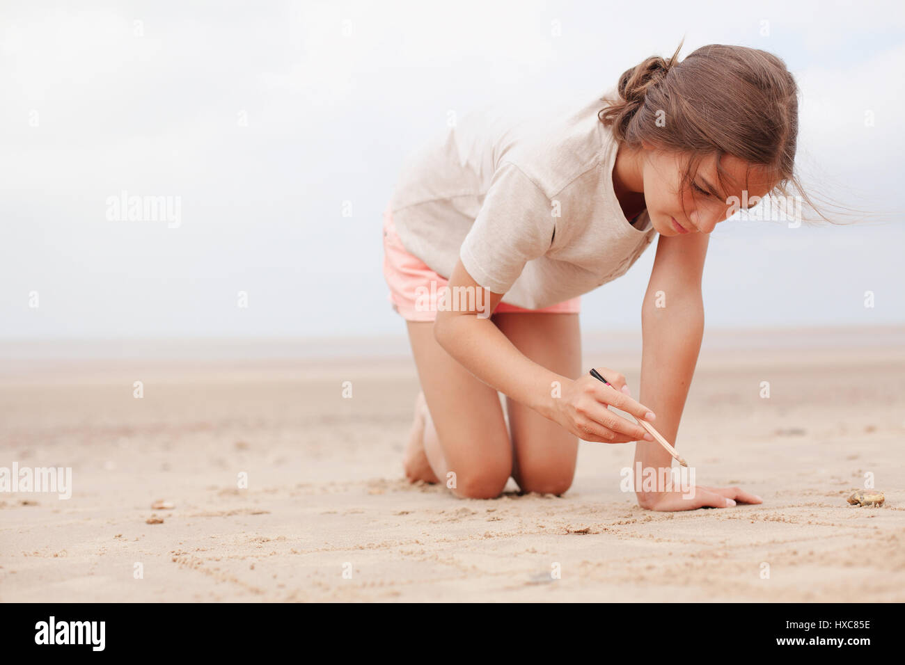 Mädchen mit Stick schreiben in Sand bedecktem Sommer Strand Stockfoto