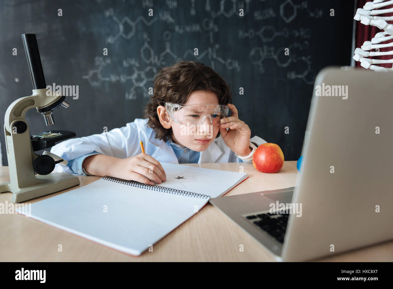 Neue Fähigkeiten zu entwickeln. Aufmerksame gescheit schlaue junge sitzen im Labor und Wissenschaft Lektion während Makig Notizen und Verwendung von Geräten Stockfoto