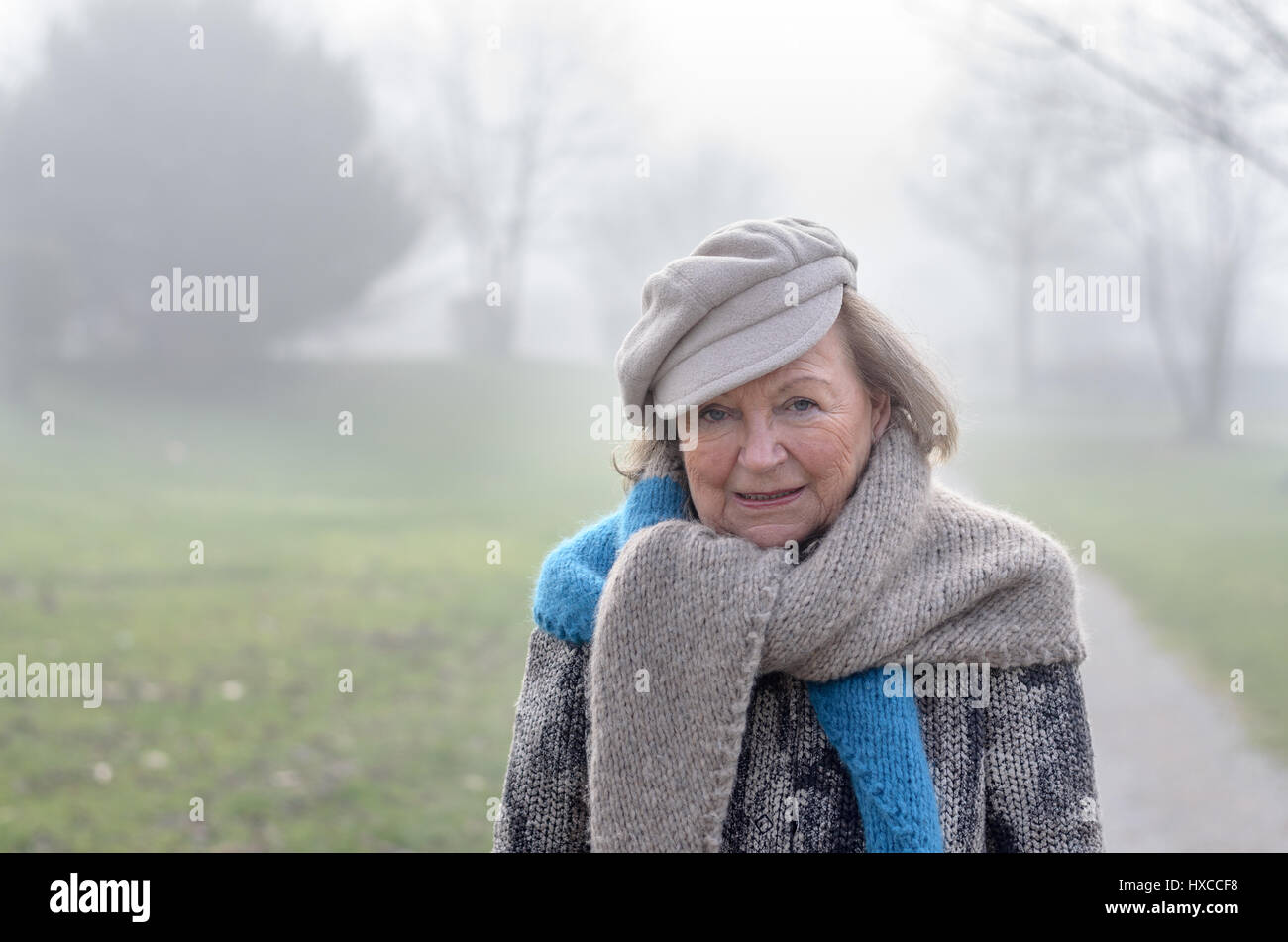 Stilvolle alte Frau trägt einen grauen Schal und Mütze zu Fuß auf einem Feldweg an einem kalten, nebligen Wintertag Nahaufnahme Kopf und Schultern Stockfoto