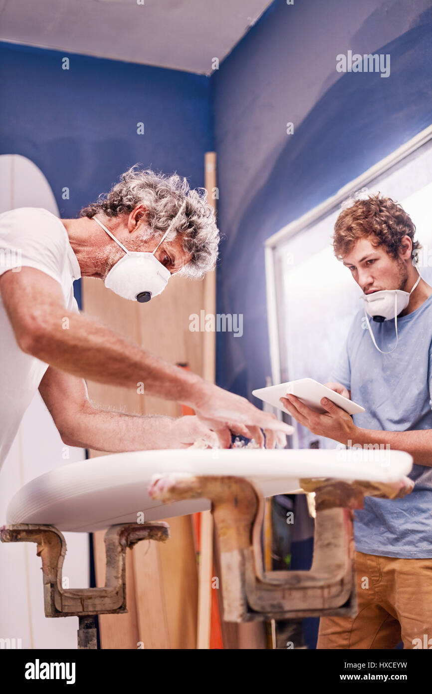 Männliche Surfbrett Designer das Tragen von Schutzmasken surfboard Schleifen in der Werkstatt Stockfoto