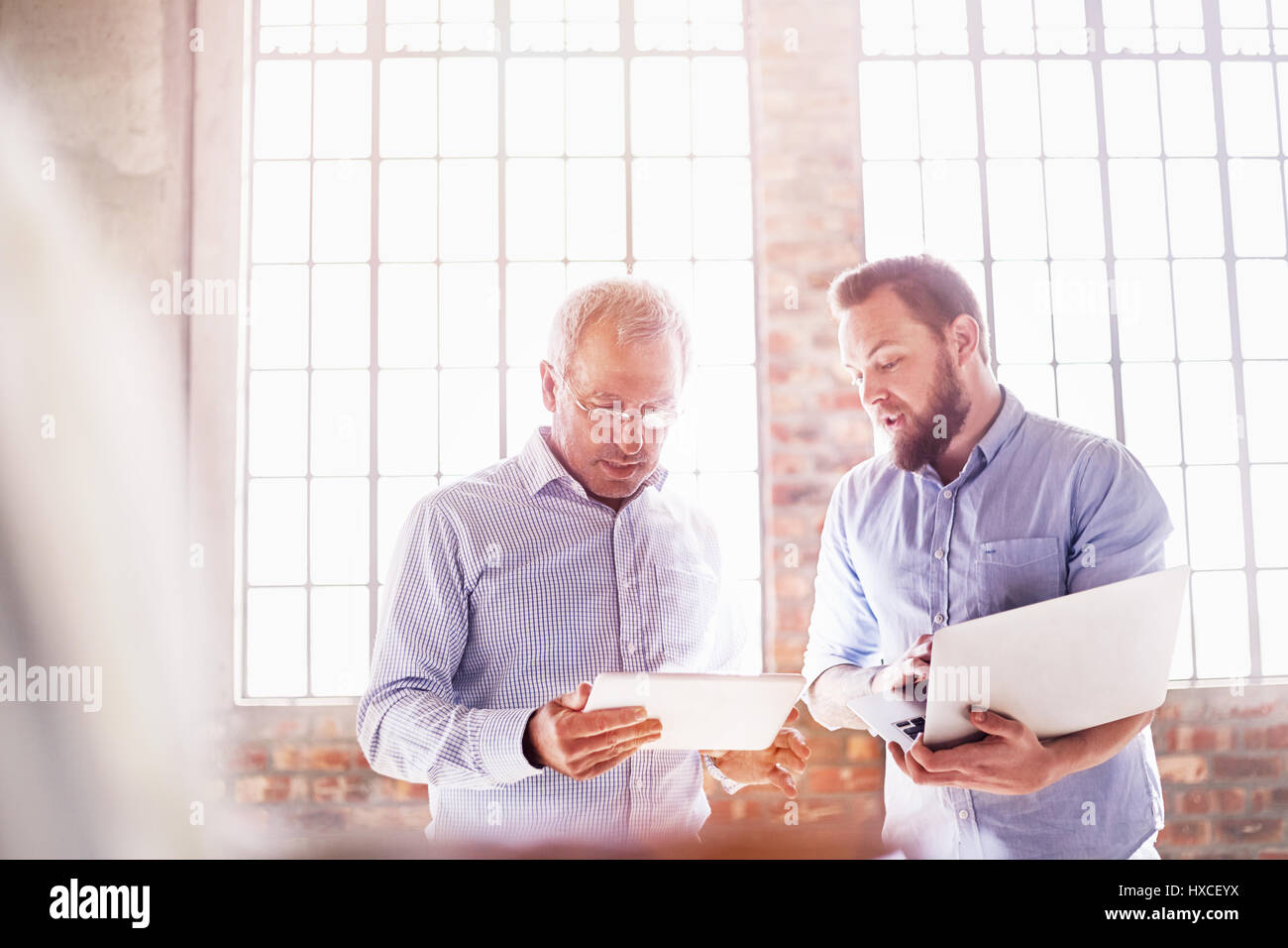 Geschäftsleute mit Laptops und digitale Tablet arbeiten im sonnigen Büro Stockfoto