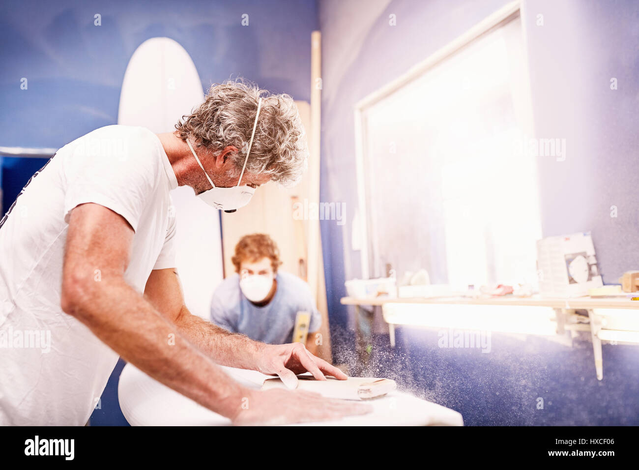 Männliche Surfbrett Designer das Tragen schützender Maske schleifen Surfbrett in Werkstatt Stockfoto