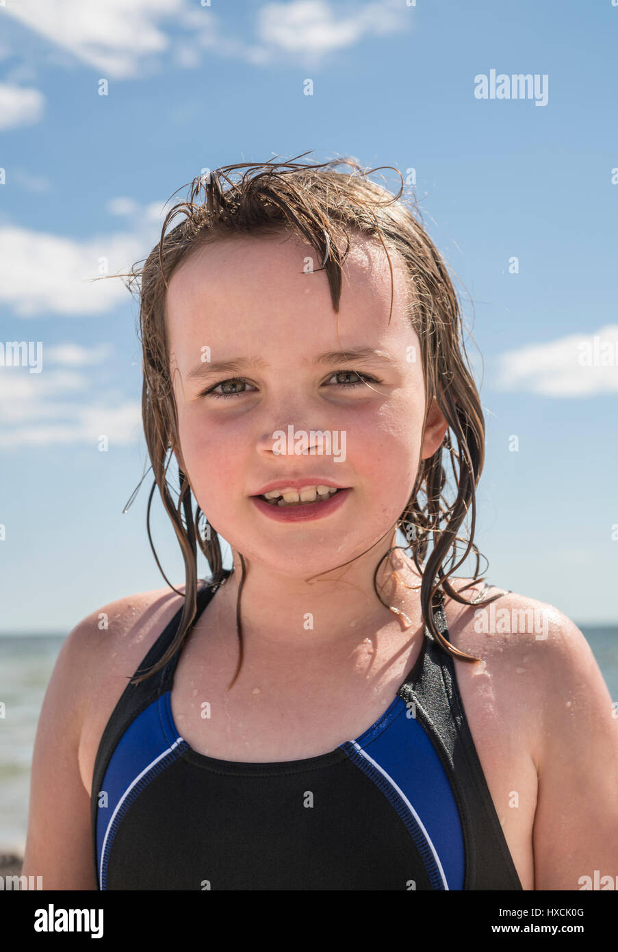 Porträt von einem nassen jungen Mädchen im Badeanzug am Strand im Sommer. Das Gesicht nur mit klarer blauer Himmel mit weißen Wolken. Stockfoto