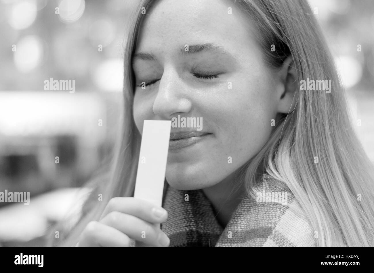 Junge, blonde Frau genoss ein Aroma mit einem schönen Lächeln der Glückseligkeit und Augen vor Lust geschlossen, da sie an eine weiße Karte in der Hand schnuppert Stockfoto