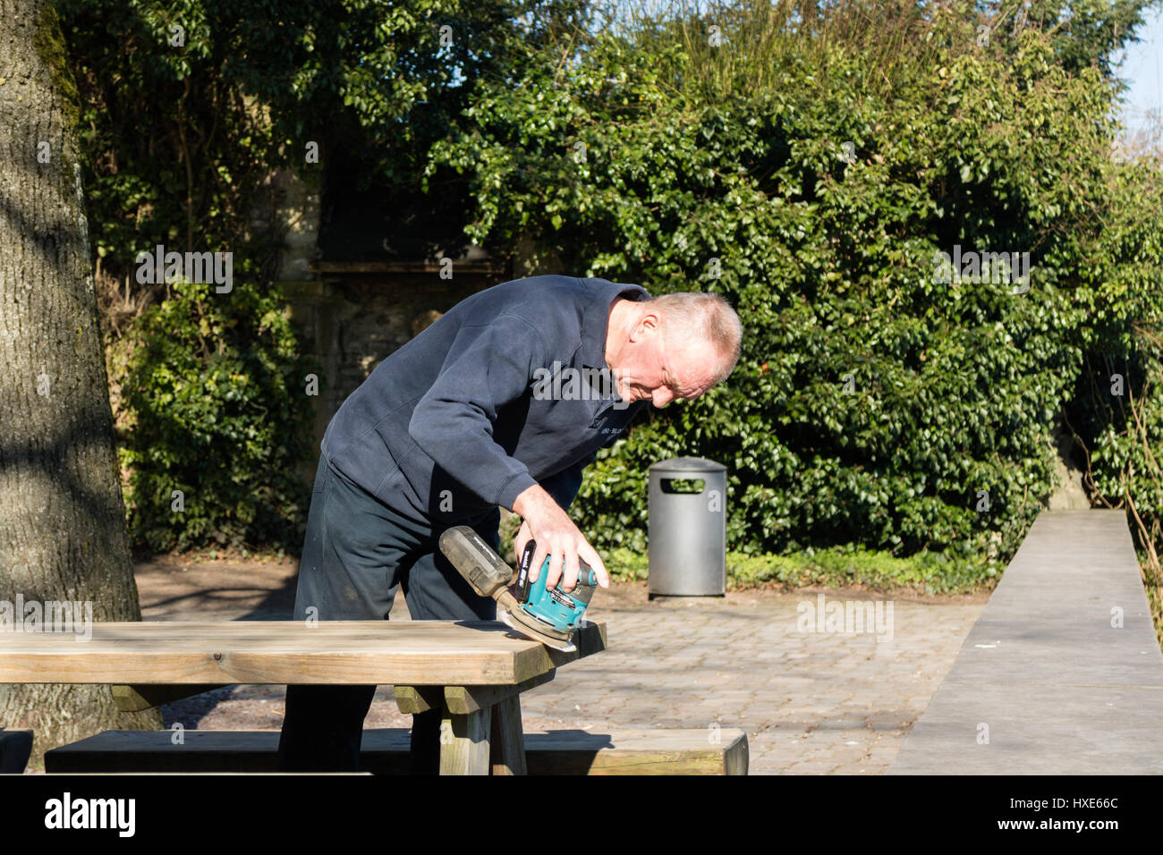 Mann bereitet Picknick Bänke/Tische durch Reinigung mit Schleifmaschine, bereit für Kunden wie Sommer naht Stockfoto