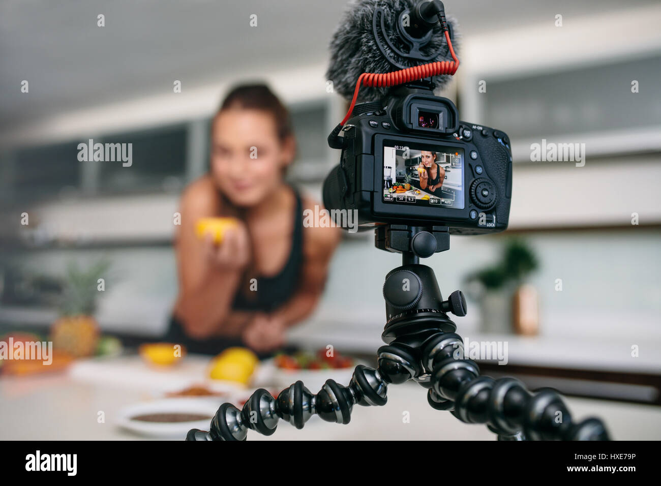 Junge Frau Videoaufnahme auf Stativ montierten Kamera in Küche. Kamera zeigt Frau mit einer Orange in der hand. Stockfoto