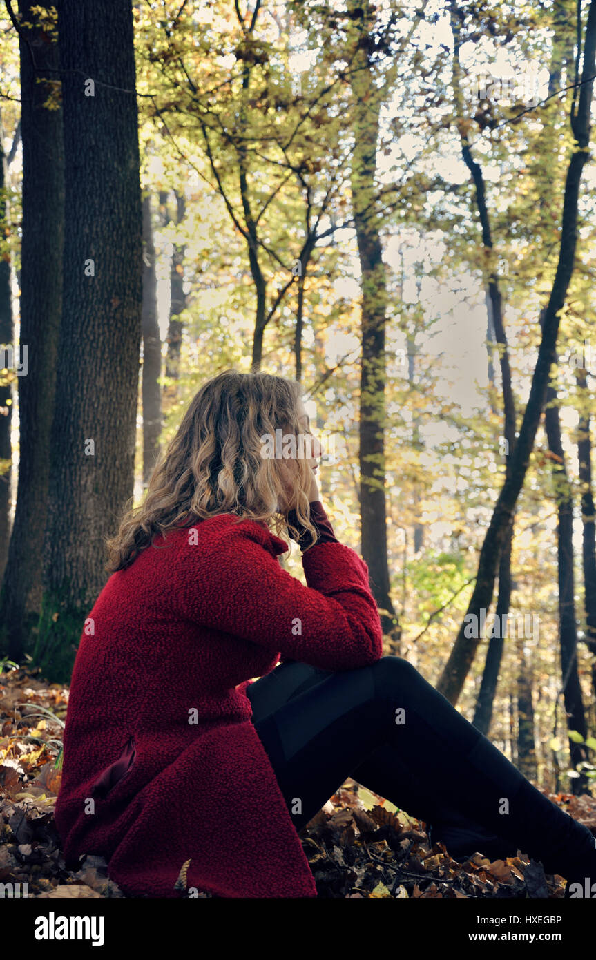 Junge Frau sitzt allein im Wald Stockfoto