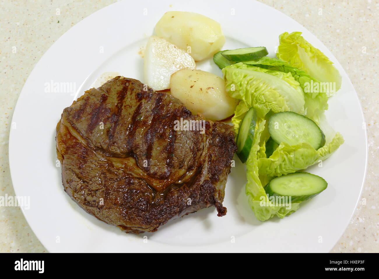 Eine Mahlzeit mit gegrillten oder gebratenen Ribeye Steak serviert mit gekochten Kartoffeln und grünem Salat Stockfoto