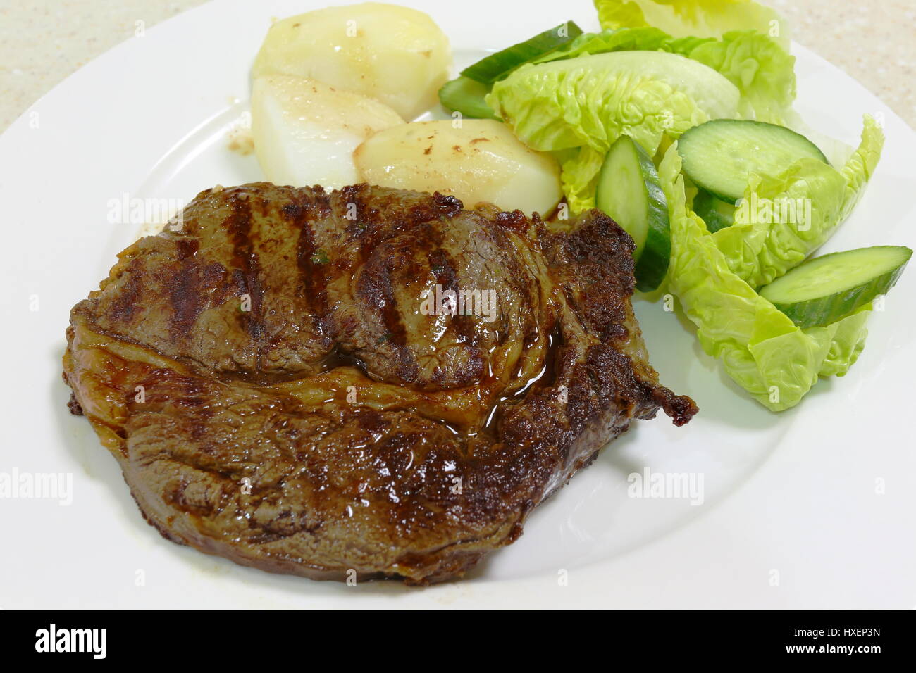Eine Mahlzeit mit gegrillten oder gebratenen Ribeye Steak serviert mit gekochten Kartoffeln und grünem Salat Stockfoto