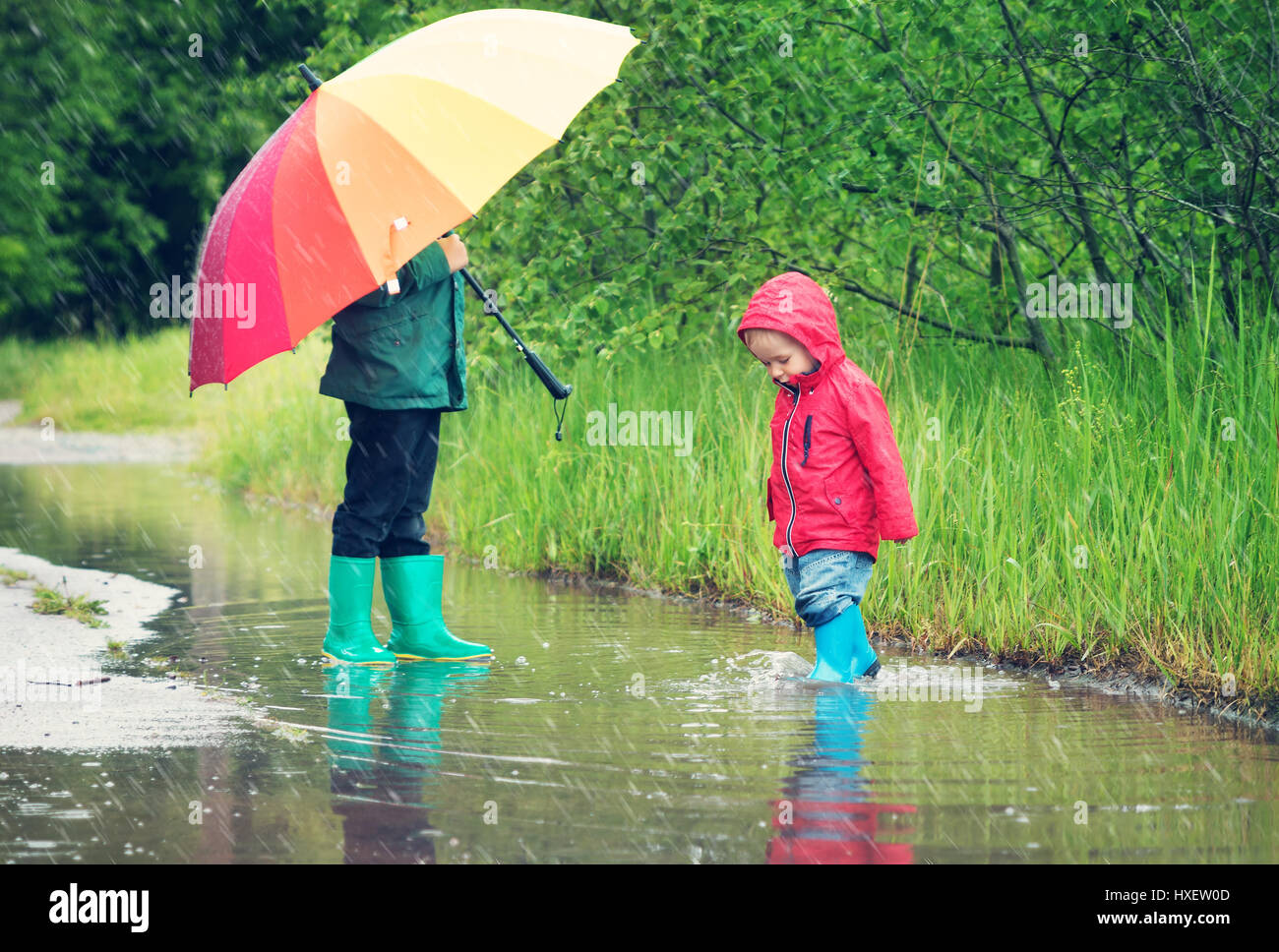 Kinder Wandern in Gummistiefel in Pfütze auf Regenwetter Stockfoto