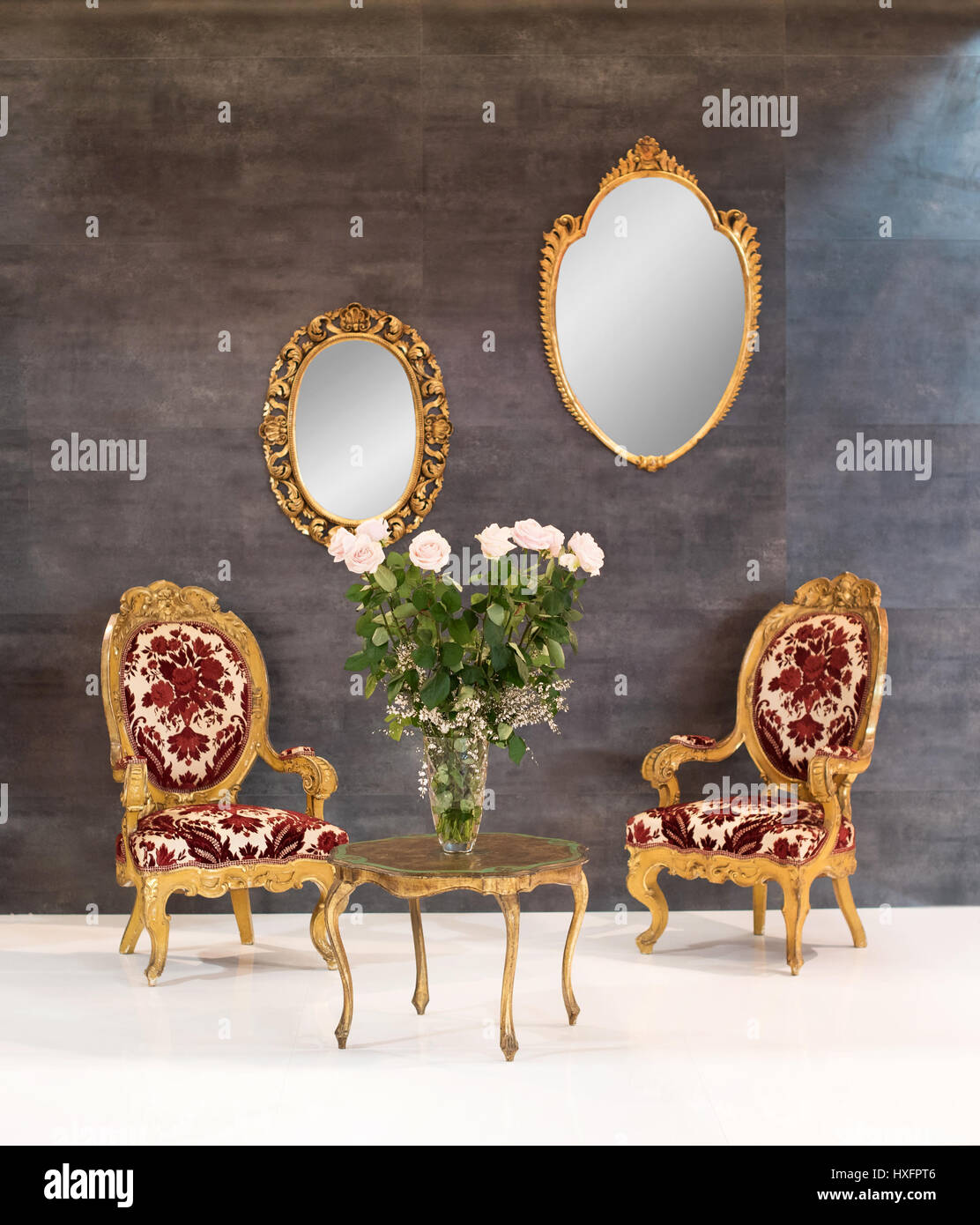 Elegante retro oder Vintage Stil Inneneinrichtung mit zwei hölzernen Polstersessel rund um einen kleinen Couchtisch mit Blumen und zwei verzierten spiegeln auf Stockfoto