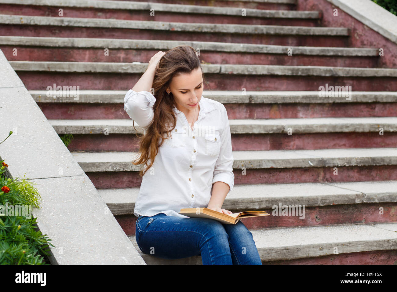 Junge Frau sitzt auf der Treppe mit Buch. Lesebuch der hispanischen Mädchen im freien Stockfoto