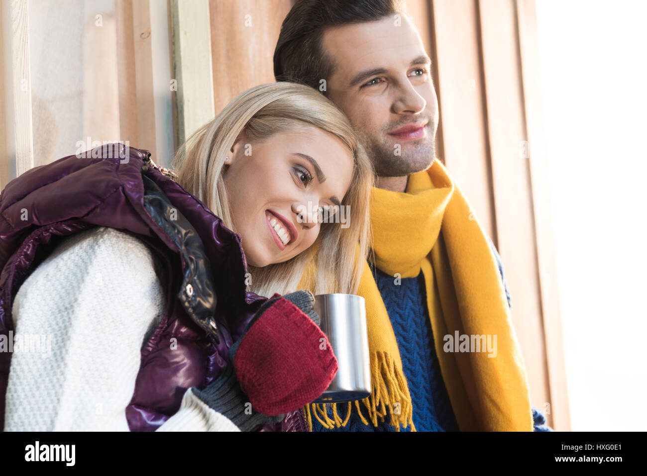 Glückliches junges Paar in warme Kleidung umarmt und wegsehen auf Veranda Stockfoto