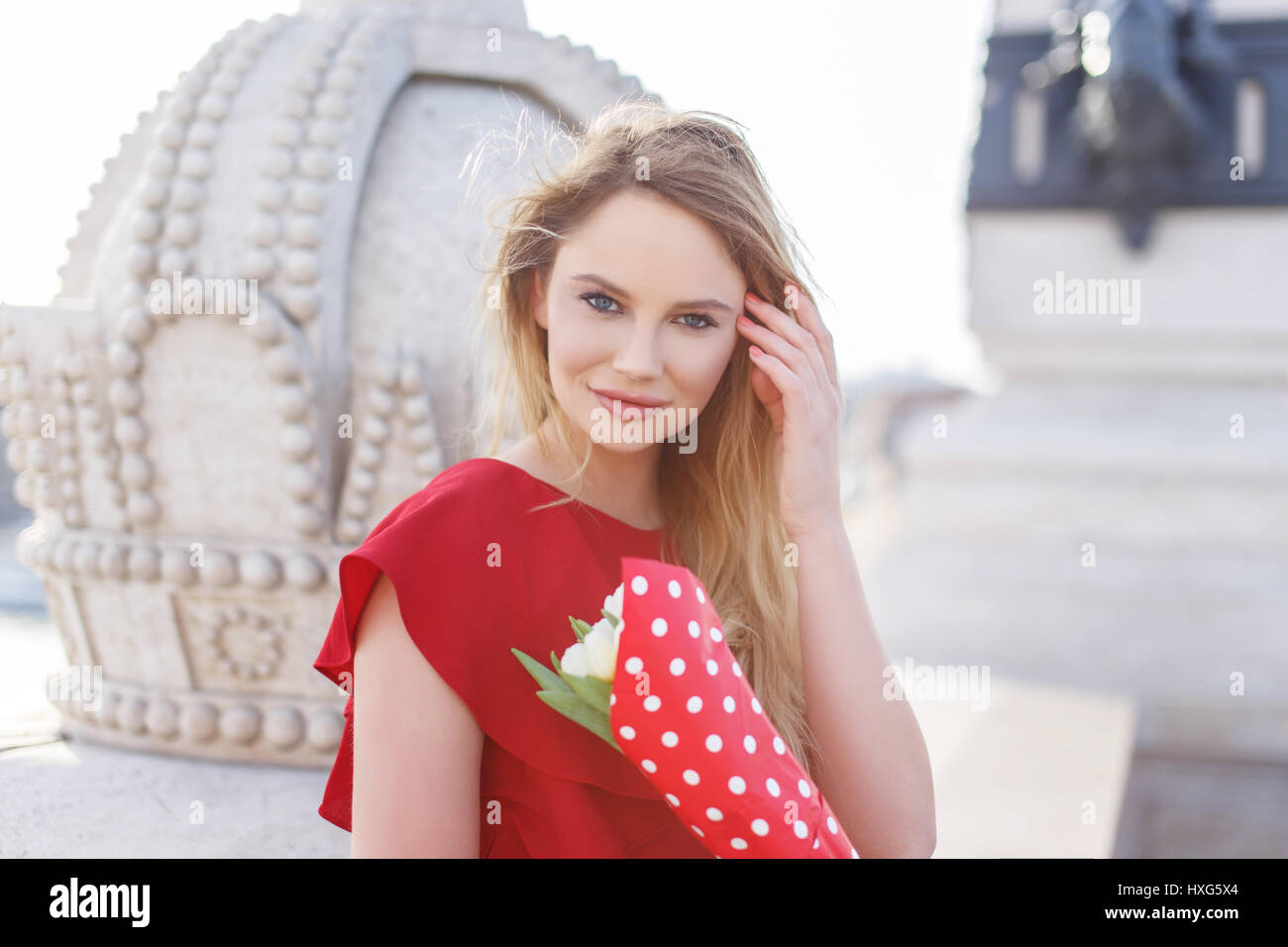 Junge blonde Kaukasische Frau im roten Kleid mit Blumenstrauß Porträt Stockfoto
