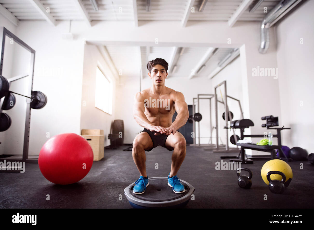 Junge fit hispanic Mann übt, macht Kniebeugen auf Fitness-Ball im Crossfit Gym. Stockfoto