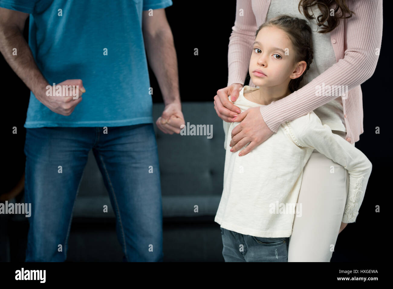 Porträt der Tochter umarmt Mutter mit aggressiven Vater hinter auf schwarz, familiäre Gewalt-Konzept Stockfoto