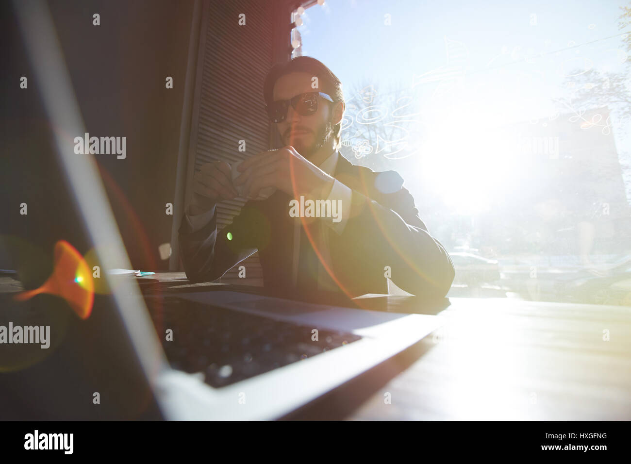 Porträt von cool Mann im Anzug arbeiten mit Laptop im sonnigen Café, große Sonnenbrille und Kaffee trinken Stockfoto