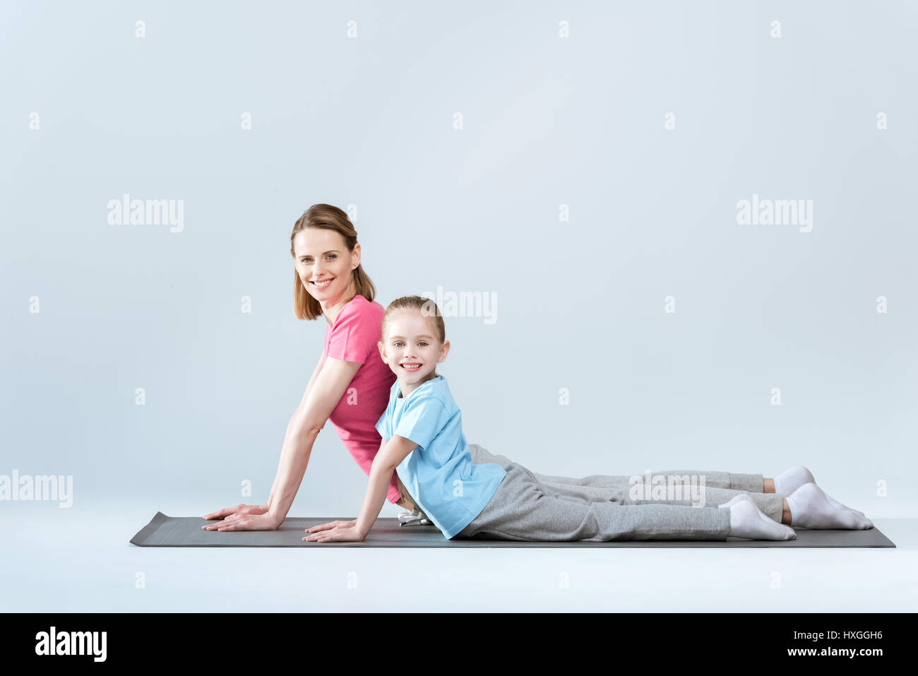 Seitenansicht des Lächelns sportliche Mutter und Tochter üben nach oben vor Hund Yoga pose auf weiß Stockfoto