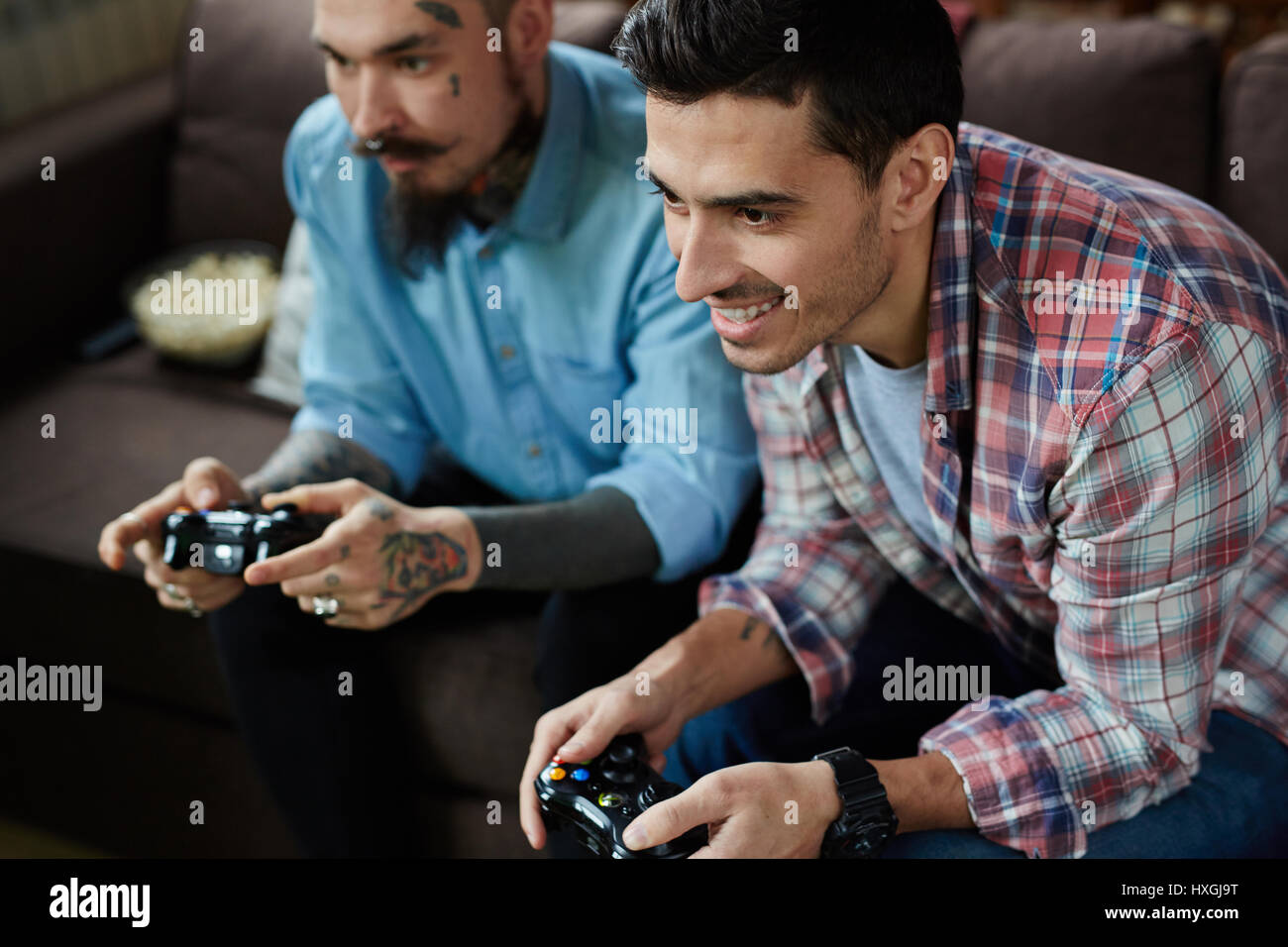 Porträt von zwei Erwachsene Männern, einer von ihnen stark tätowiert, genießen Videospiel-Wettbewerb und lächelte freudig Holding Controller während Sitti begeistert Stockfoto