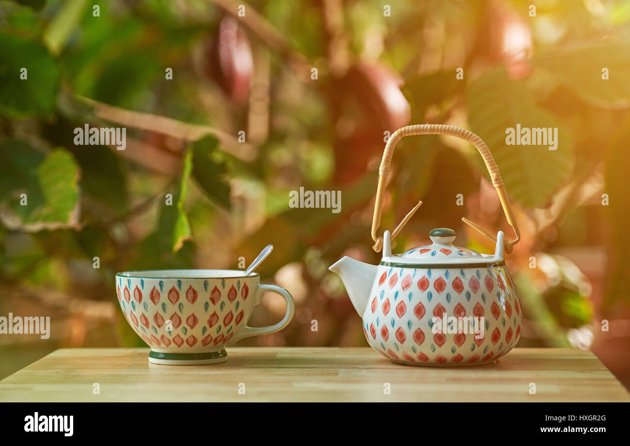 Teetasse und Topf stehen auf Holztisch mit Baum mit Kulturen verschwimmen Hintergrund Stockfoto