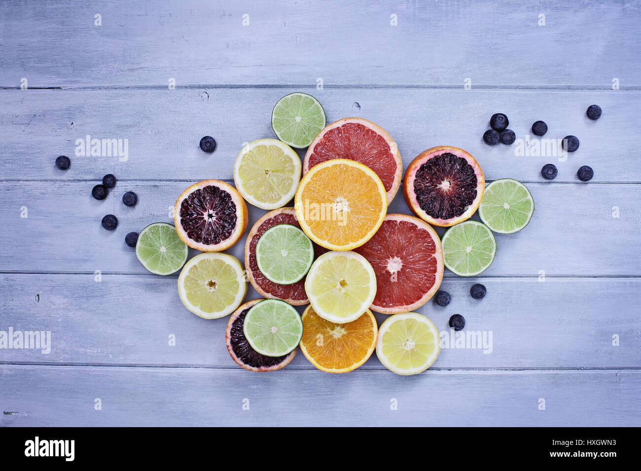 Vielzahl von Zitrusfrüchte (Orange, Blutorangen, Zitronen, Grapefruit und Limetten) mit Heidelbeeren über eine blaue rustikale Holz Tischplatte. Bild von o Stockfoto