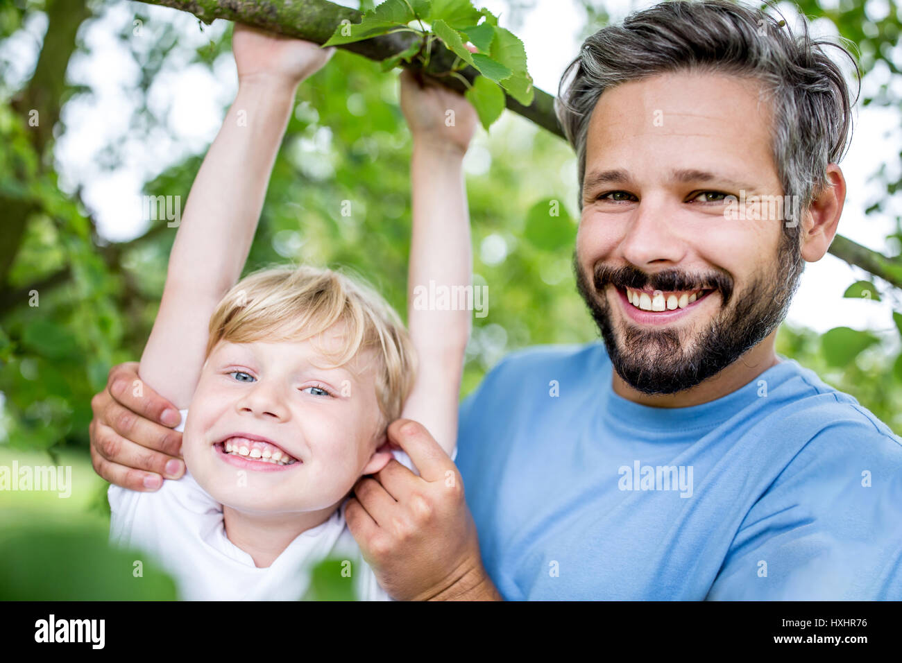 Vater unterstützt Sohn mit Gymnastik, während junge Baum klettert Stockfoto