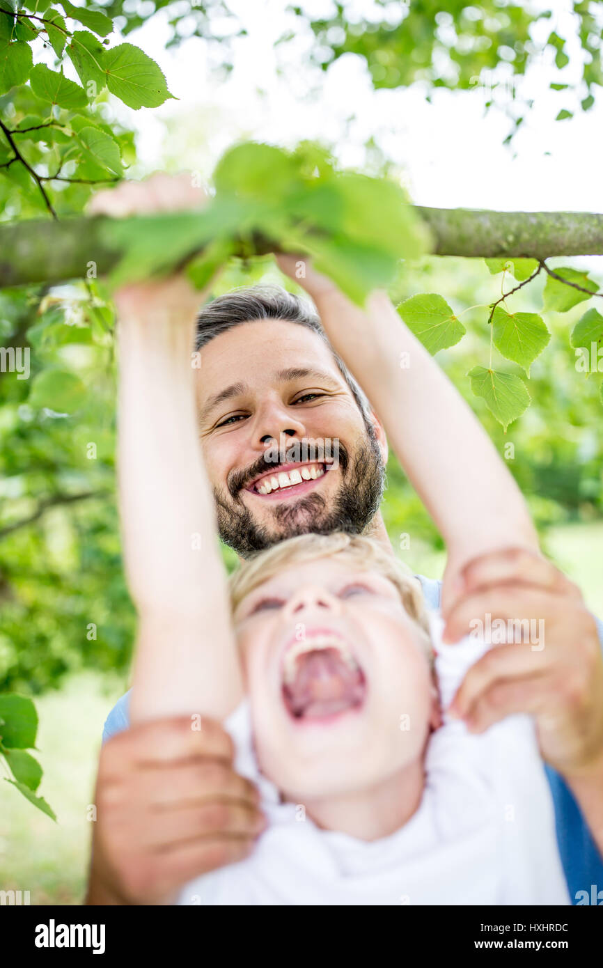 Vater Sohn Aufstieg Baum hilft und sie Spaß haben, Lachen im Sommer Stockfoto