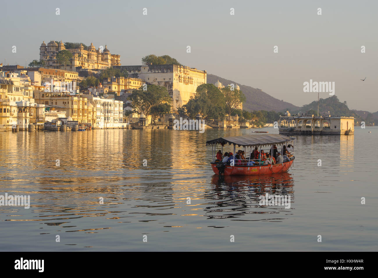 Ein Boot nimmt die Besucher mit auf die Udaipur Lake Pichola, City Palace als Hintergrund Stockfoto