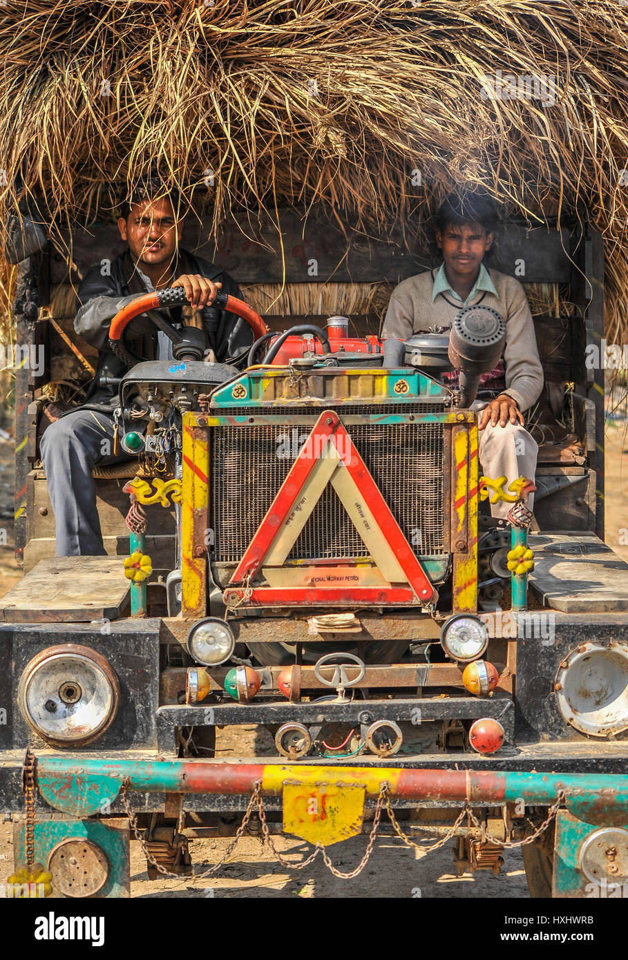 Fahrer und seinem Kumpel sitzen in einem cabinless LKW beladen mit Elefantengras, Indien Stockfoto