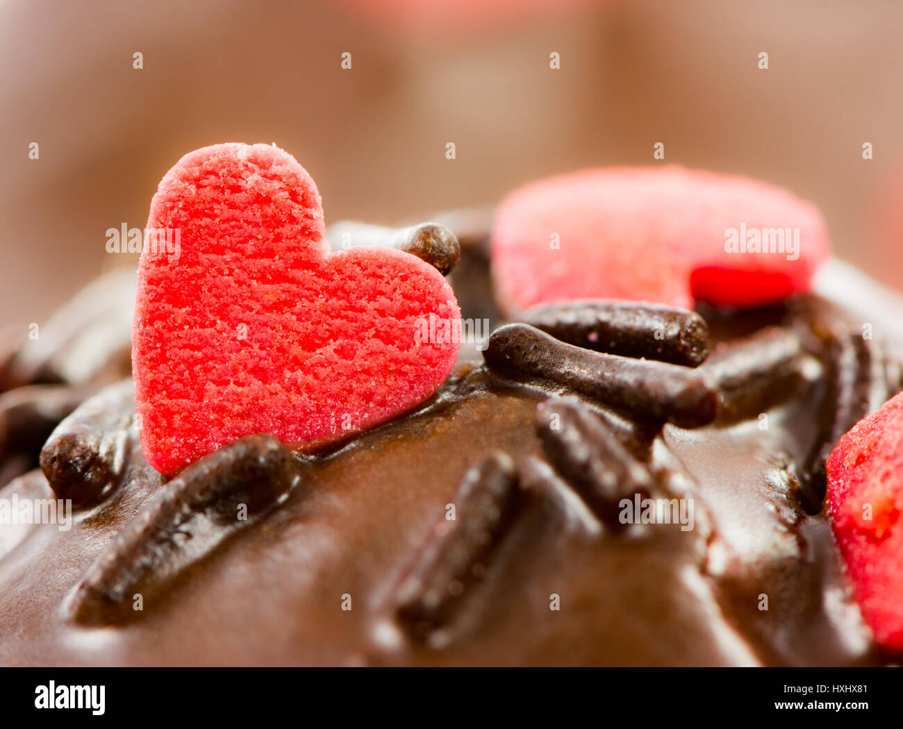 Detail von einem Schoko-Muffin mit roten Zuckerherzen und Streuseln Stockfoto