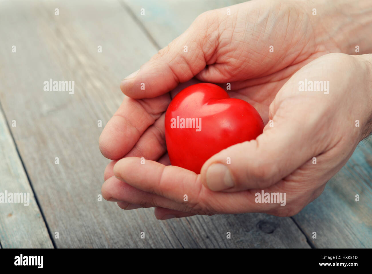 Männerhände mit dekorativen Stein Herz über hölzerne Hintergrund Stockfoto