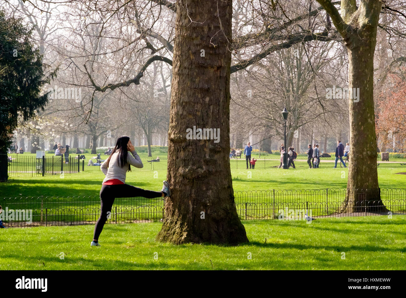 Eine Frau tut erstreckt sich im St. James Park in London während des Gesprächs auf ihrem Mobiltelefon Stockfoto