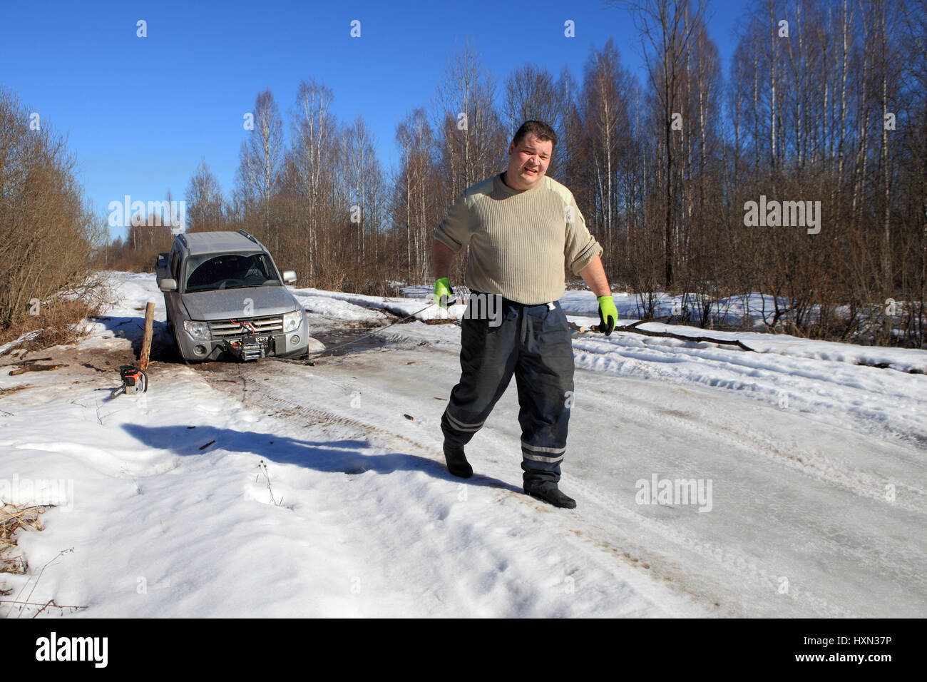Nazia Village, Leningrad Region, Russland - 17. März 2015: Auto stecken auf einem Waldweg, Vorderrad verfiel Schlucht im Eis, der Mann zieht das Kabel Stockfoto