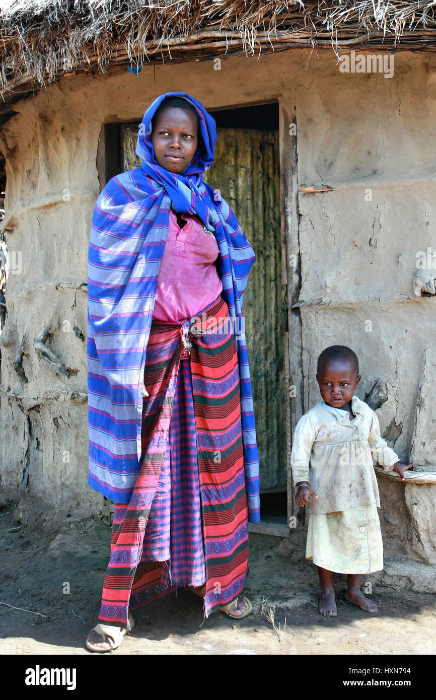 Meserani Snake Park, Arusha, Tansania - 14. Februar 2008: Junge Frau Massai Stamm in drapierten Gewand und ein kleines Mädchen stand vor seinem Haus, Stockfoto