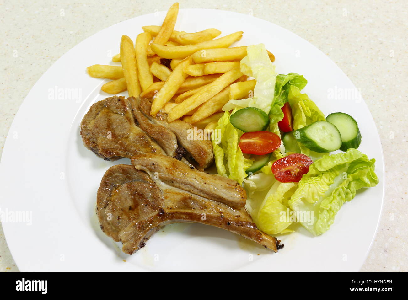 Zwei Gegrillte Lammkoteletts serviert mit französischer gebratene Kartoffelchips und Salat aus Kopfsalat, Tomaten und Gurken. Stockfoto