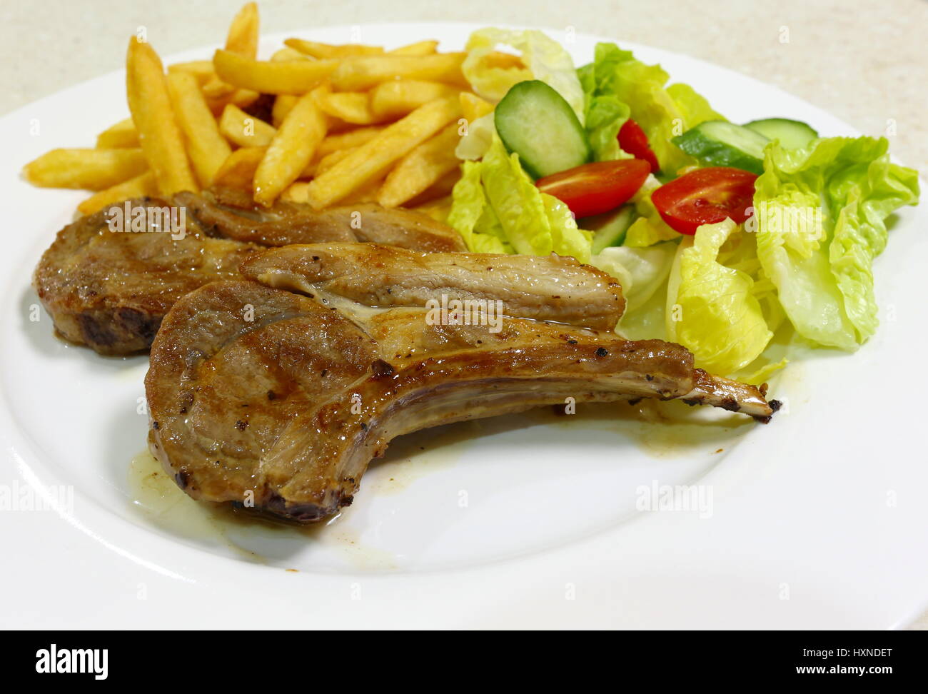 Zwei Gegrillte Lammkoteletts serviert mit französischer gebratene Kartoffelchips und Salat aus Kopfsalat, Tomaten und Gurken. Stockfoto