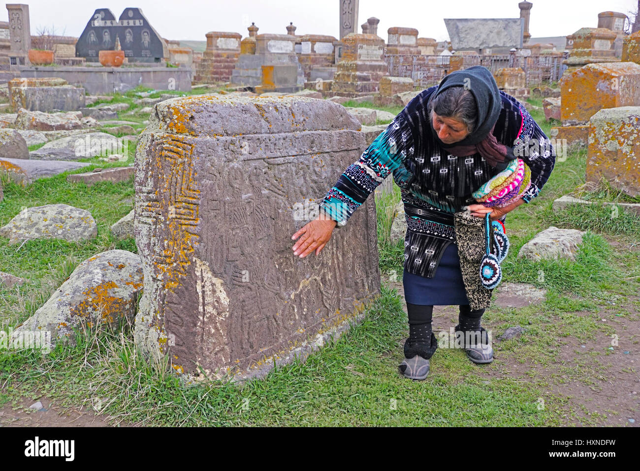 Armenische Frau zeigt Schnitzereien in ein Katchkar Grab aus Stein in Noraduz Friedhof. Stockfoto