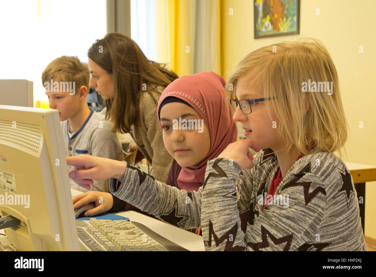 Kinder in der Grundschule, die Arbeit mit einem Computer, ihre Lehrer, die ihnen helfen Stockfoto