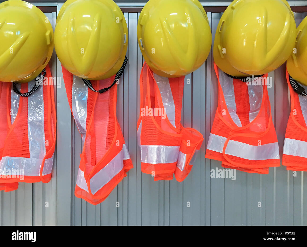 Reihe neuer Helm und Jacke hängt an der Bürowand für den Einsatz der Vorarbeiter auf der Baustelle. Stockfoto