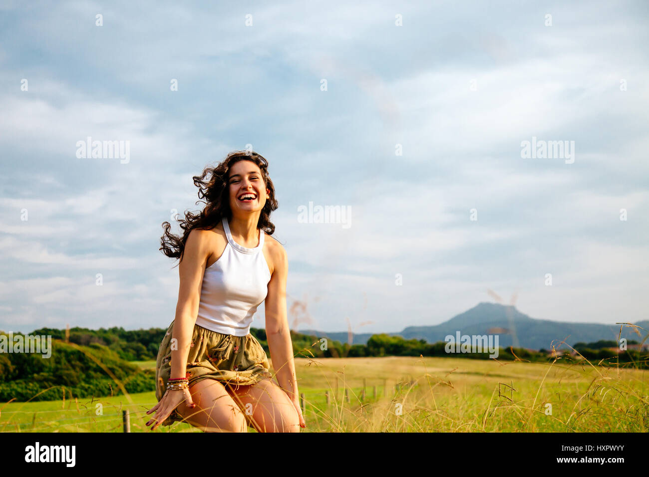 Junge Frau in einer grünen Landschaft an einem sonnigen Tag springen lachen Stockfoto