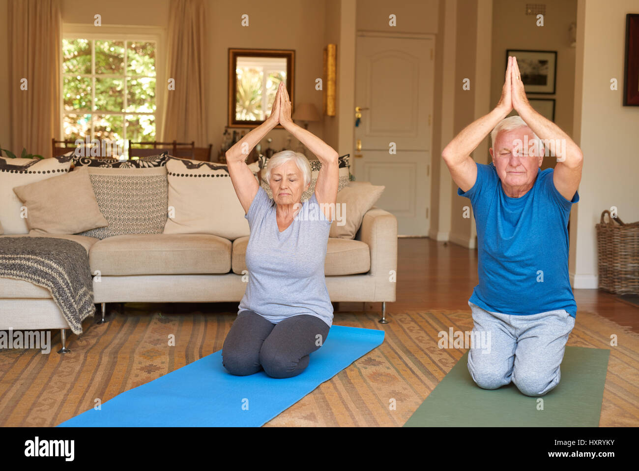 Aktive Senioren paar praktizieren Yoga zusammen in ihrem Wohnzimmer Stockfoto