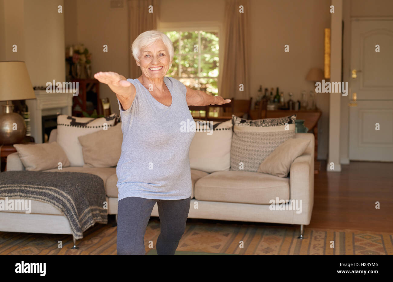 Aktive ältere Frau lächelt und macht Yoga alleine zu Hause Stockfoto