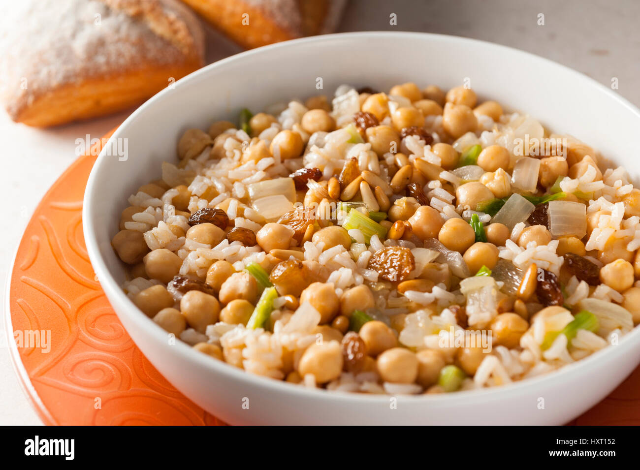 weißer Reis mit Rosinen, Pinienkernen und Kichererbsen in einer weißen Schüssel auf einem orangefarbenen Tablett mit Brötchen serviert Stockfoto