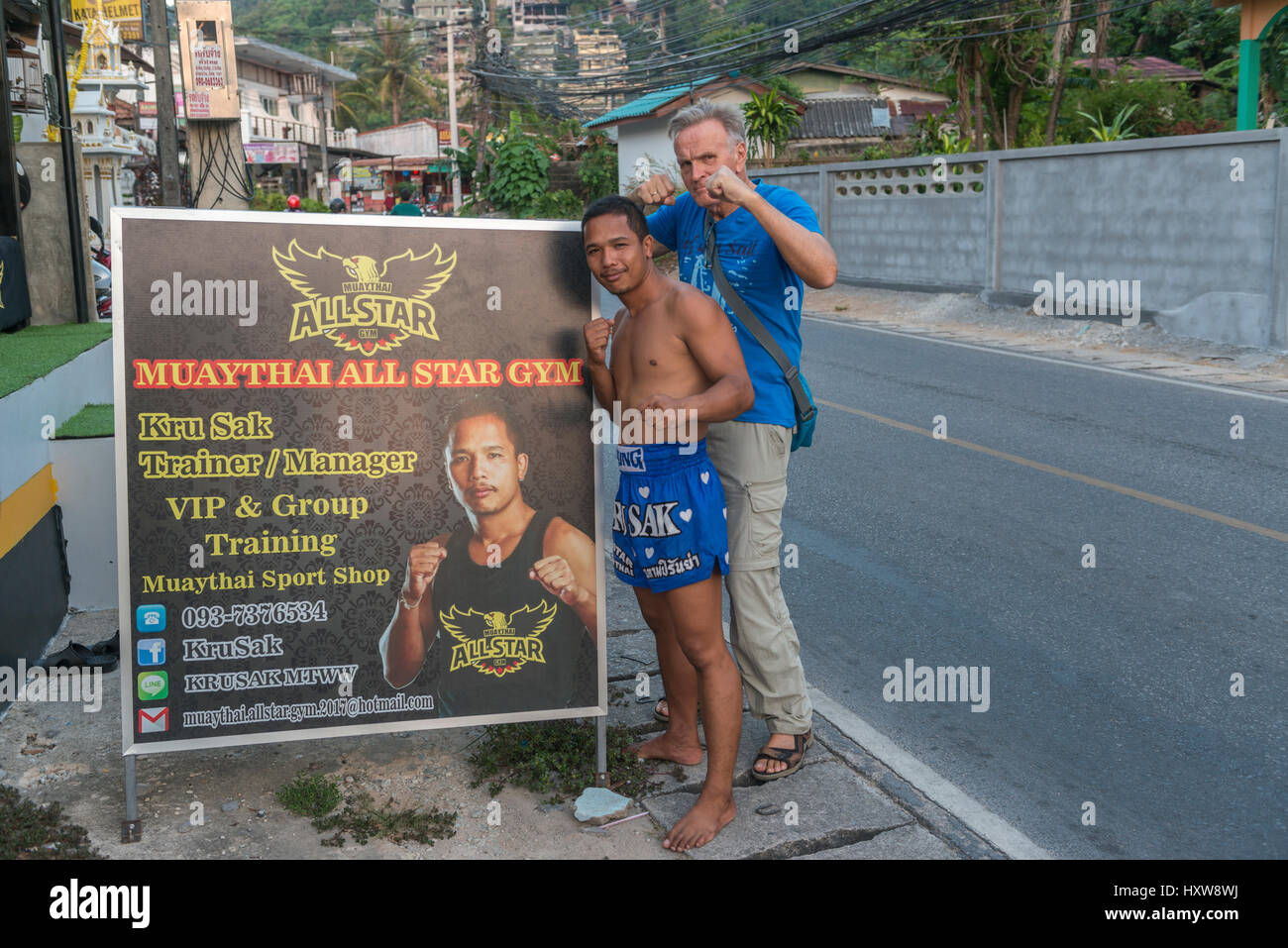 Kru Sak, eine Muay Thai oder Thai-Boxer, stellt neben einer Plakatwand Funktionen seinem Fitness-Studio während ein westlicher Tourist in Phuket, Thailand sich schließt. 9. März 2017 Stockfoto